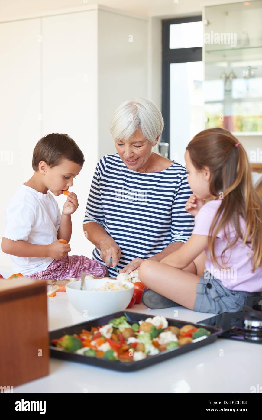 Eine Großmutter, die mit ihren Enkelkindern in einer Küche Gemüse wäscht. Stockfoto