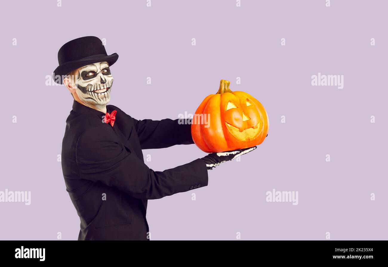 Fröhlicher Mann mit traditionellem Halloween Skelett Make-up mit leuchtendem Kürbis in seiner Handfläche. Stockfoto