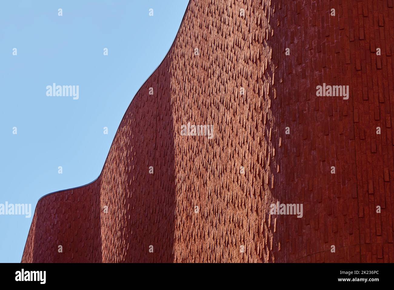 Rot-braun gewellte Ziegelwand moderner Architektur mit Licht und Schatten unter einem blauen Himmel im Sommer. Stockfoto