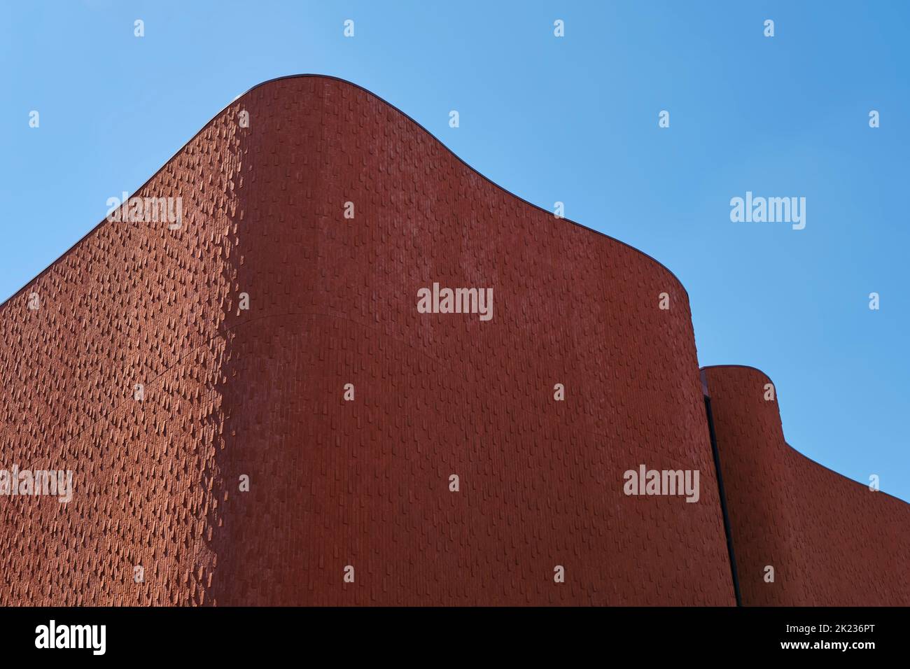 Rot-braun gewellte Ziegelwand moderner Architektur mit Licht und Schatten unter einem blauen Himmel im Sommer. Stockfoto