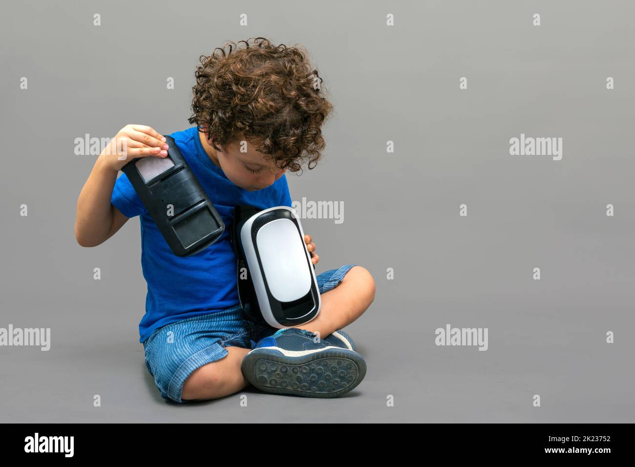 Kind mit einer Virtual-Reality-Brille in den Händen, das neugierig auf ihre Arbeitsweise schaut Stockfoto