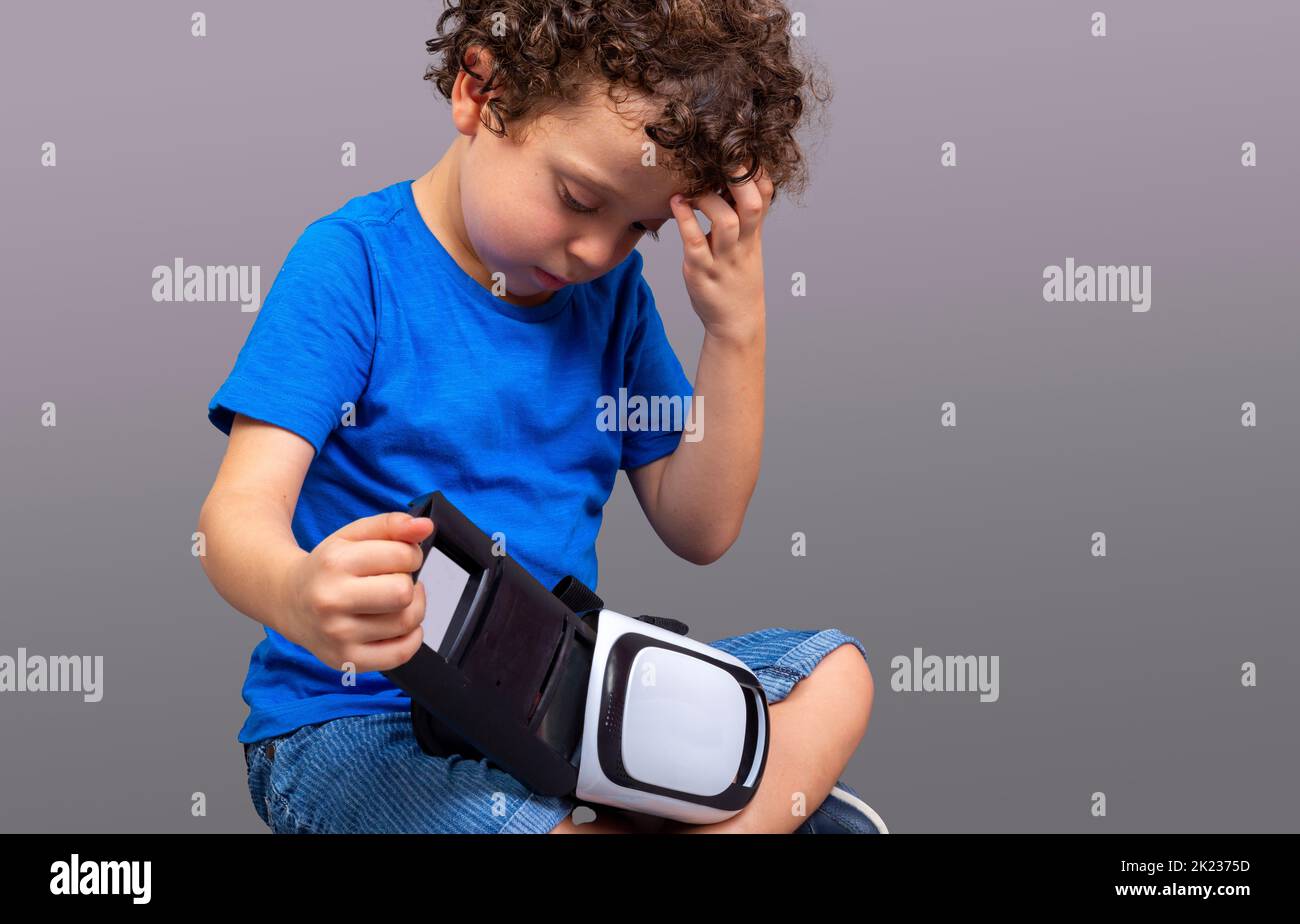 Kleiner Junge mit einer Virtual-Reality-Brille in den Händen, der neugierig auf ihre Funktionsweise schaut Stockfoto