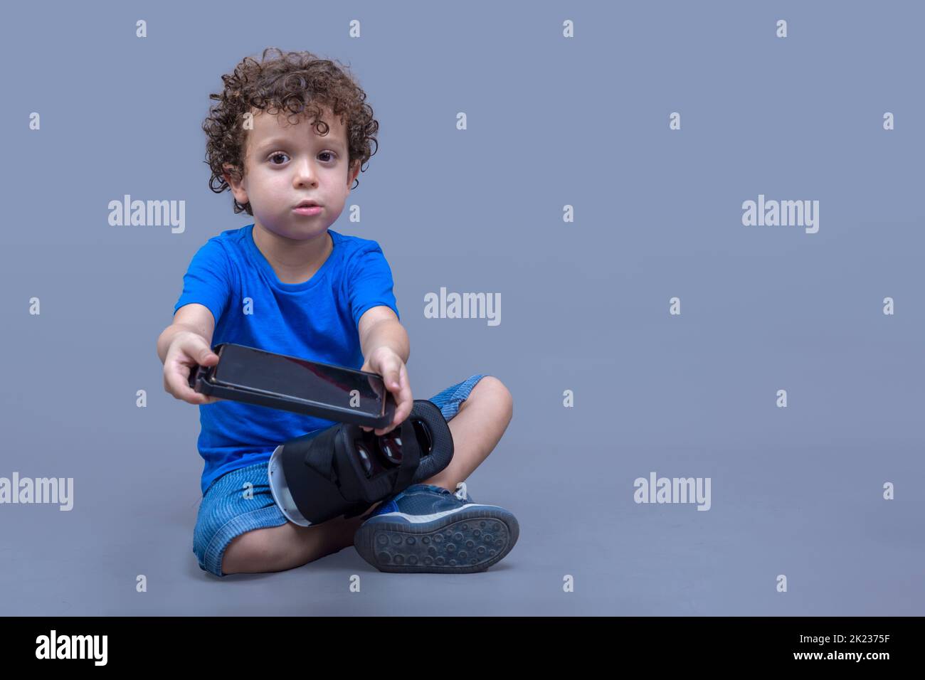 Kleiner Junge mit einer Virtual-Reality-Brille in den Händen, der neugierig auf ihre Funktionsweise schaut Stockfoto