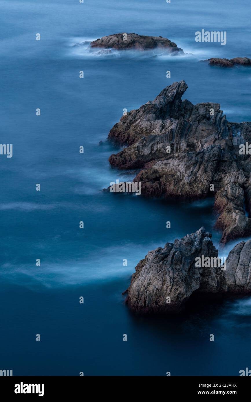 Lange Exposition von Meer und Felsen. Wellen, die auf den Felsen plätschern, schaffen ein schönes Bild. Wunderschöne Farben bei Sonnenuntergang. Asturien-Landschaft Stockfoto