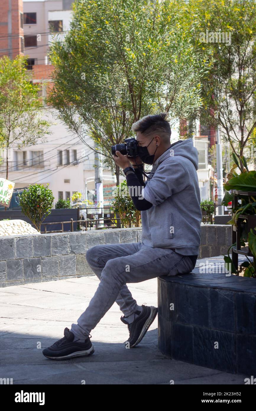 La Paz, Bolivien - 11 2022. September: Der junge bolivianische Mann mit moderner Frisur ist in Grau gekleidet und macht auf dem Hauptplatz von Miraflore ein Bild Stockfoto