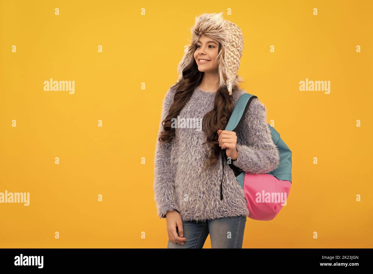 Glückliches Kind mit lockigen Haaren im Hut. Zurück zur Schule. Teen Mädchen in Strickmode auf gelbem Hintergrund. Stockfoto