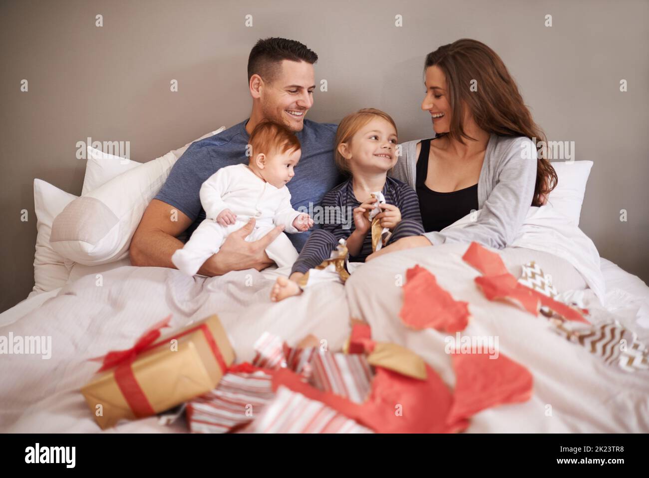 Danke Mama und Papa. Eine liebevolle junge Familie liegt im Bett und tauscht Geschenke aus. Stockfoto