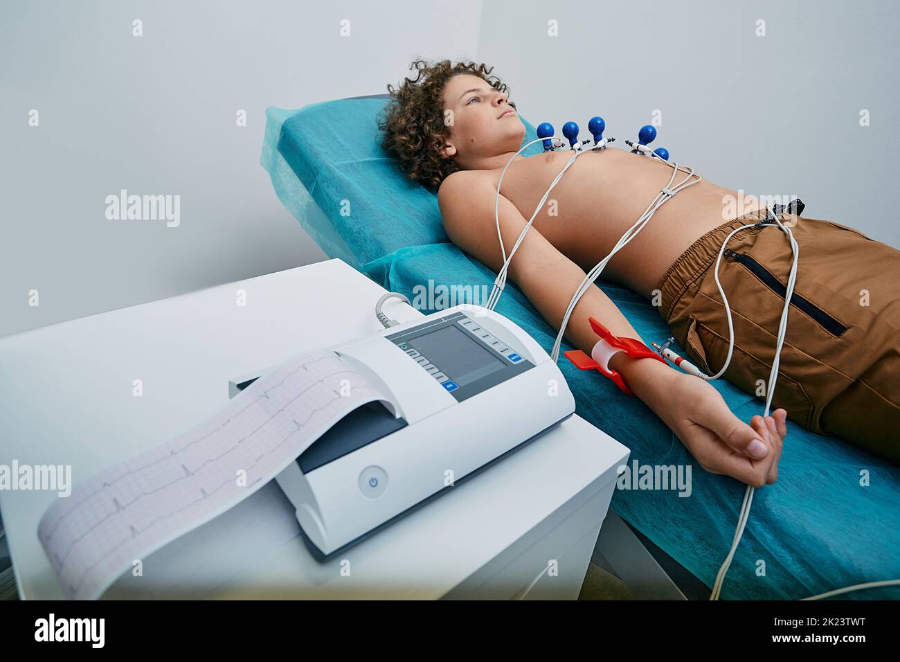 Männliches Kind, das während des EKG-Verfahrens mit Saug-Brustelektroden auf dem Bett liegt. Elektrokardiographie für Kinder Stockfoto