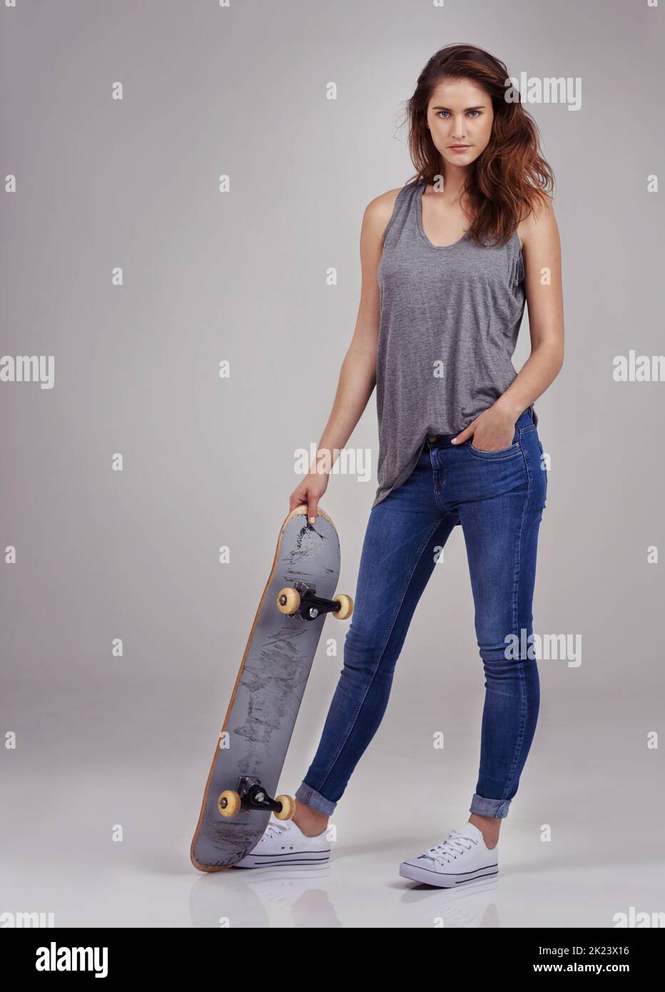 Skate betty. In voller Länge Studio-Porträt von lässig gekleideten jungen Frau auf einem Skateboard halten. Stockfoto