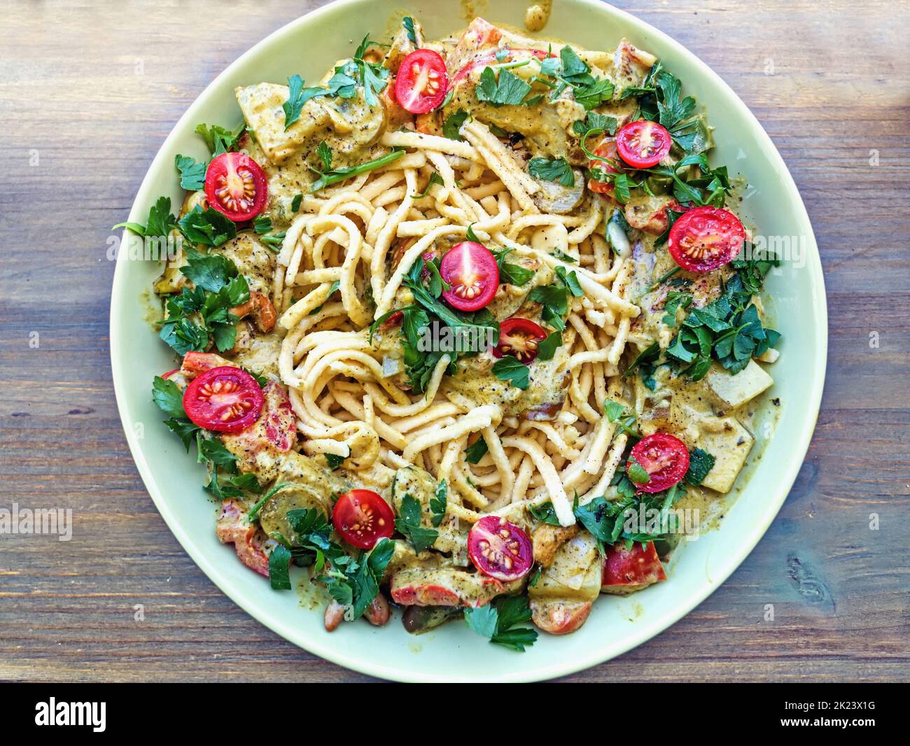 Draufsicht auf einen Teller mit Spätzle, umgeben von einem Rand aus Gemüsekerl, frischen Kräutern und halbierten Kirschtomaten. Stockfoto