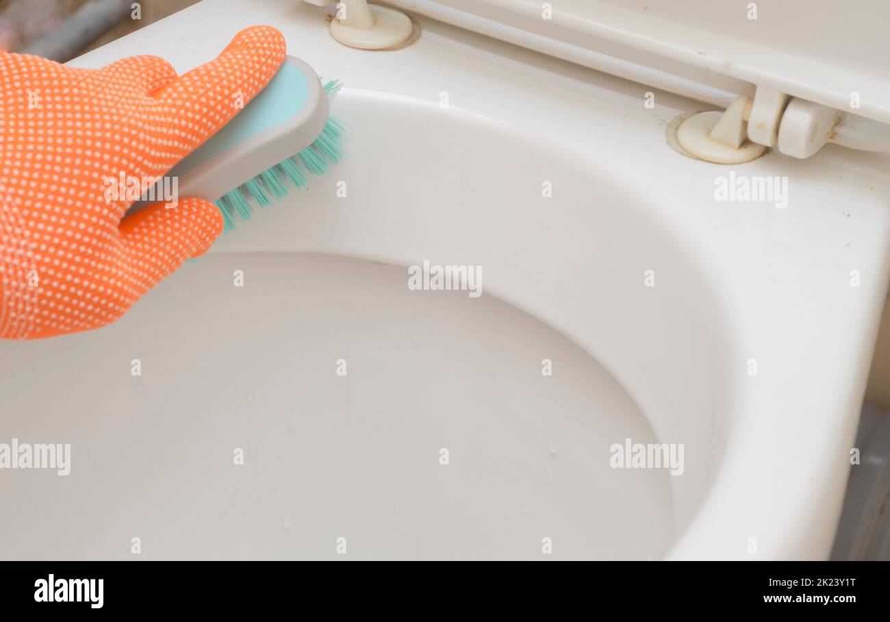 Mann Hand in orange Handschuh mit einer Bürste reinigt Toilette. Stockfoto