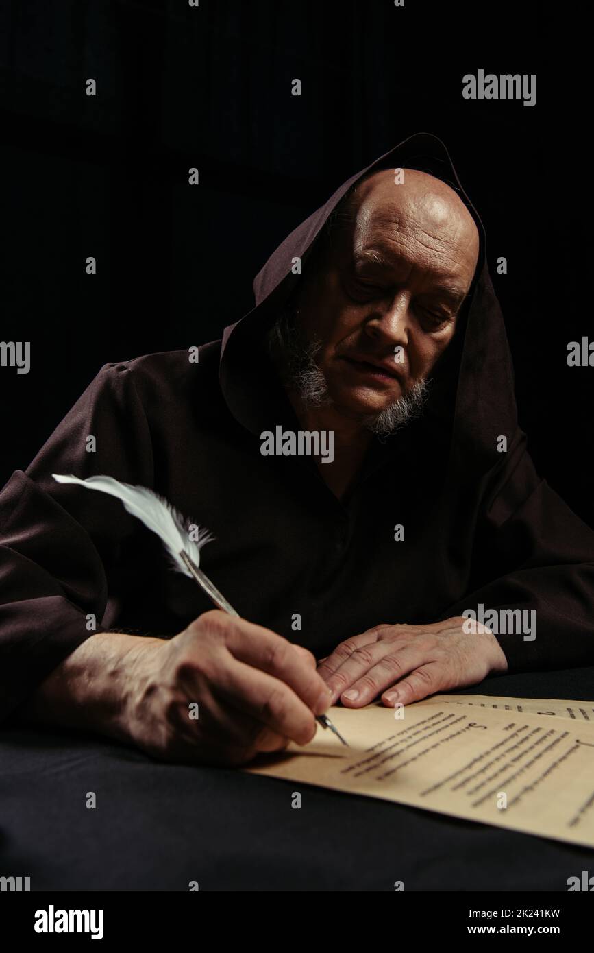 Älterer mittelalterlicher Priester, der alte Chronik auf Pergament schreibt, isoliert auf schwarzem, Stockbild Stockfoto