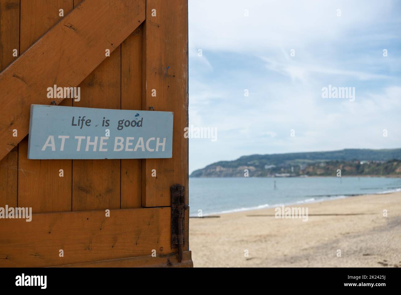 Das Leben ist gut am Strandschild an einer Tür mit einem Strand, der außer Fokus steht. Stockfoto