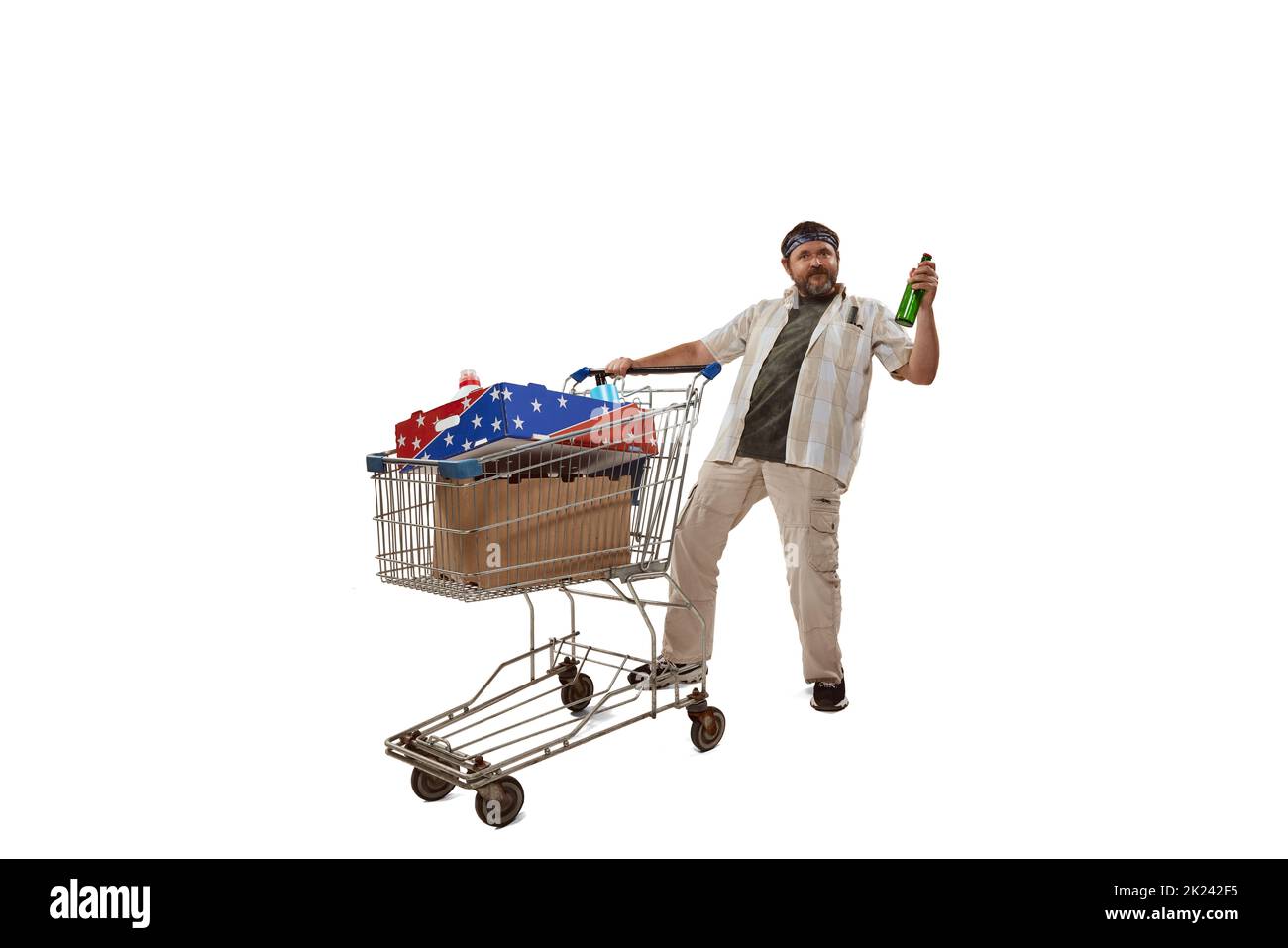 Fröhlicher Mann in legerer Kleidung beim Einkaufen, mit einem großen Einkaufswagen mit Waren stehend, Bier haltend Stockfoto