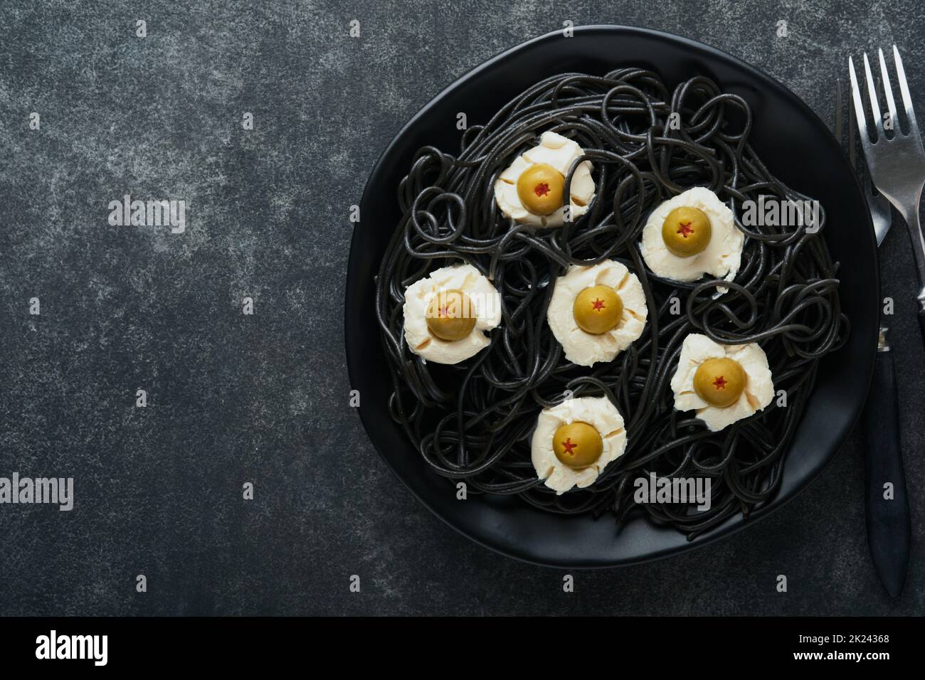 Halloween Party italienische schwarze Pasta dekoriert Horror Oliven wie Augen auf schwarzem Teller auf alten dunklen Tisch Hintergrund. Monster Gesicht von Pasta. Halloween Stockfoto