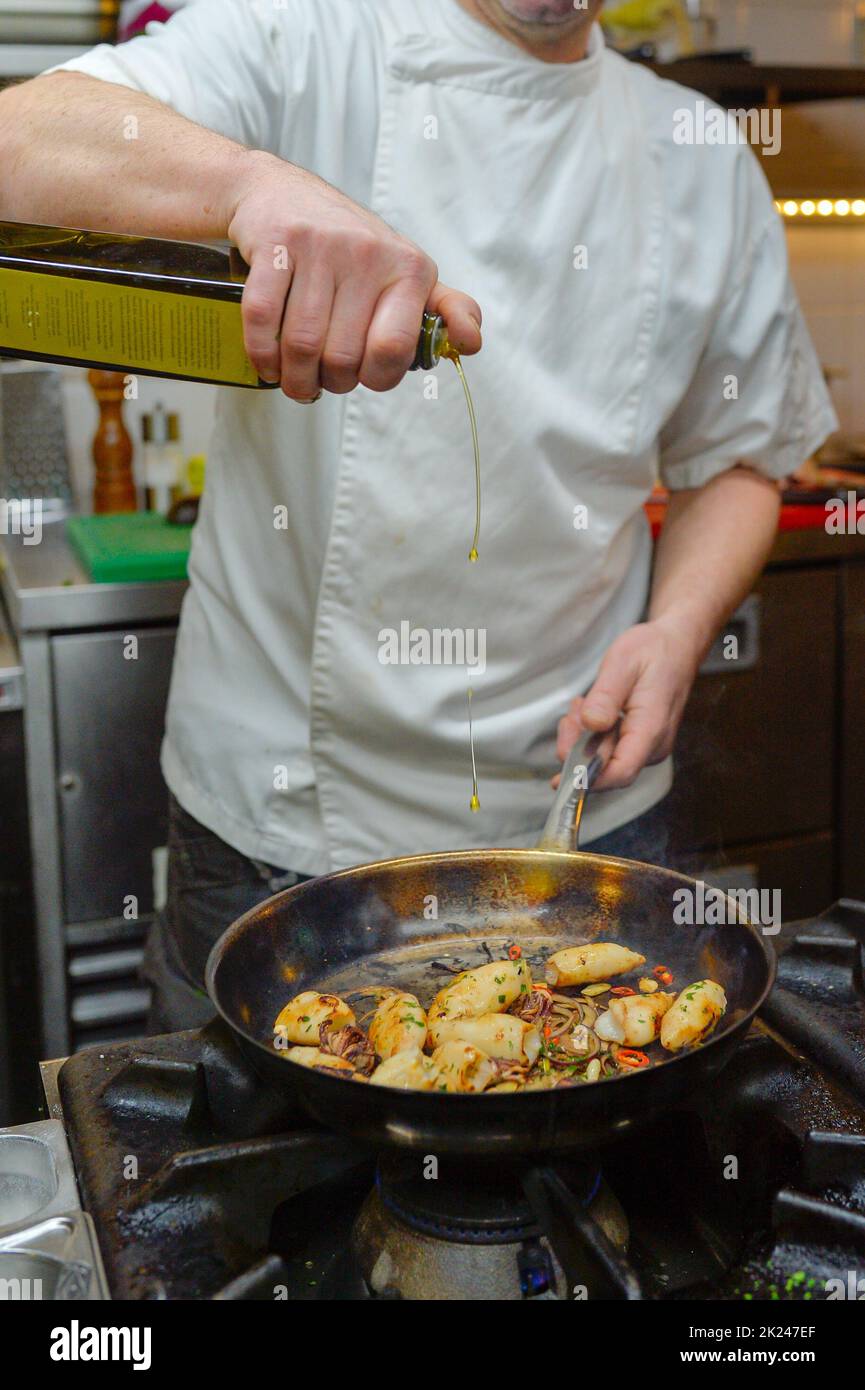 In einer Restaurantküche werden Calamari vom Küchenchef auf einem Gasherd gegrillt und mit Olivenöl verfeinert. Stockfoto