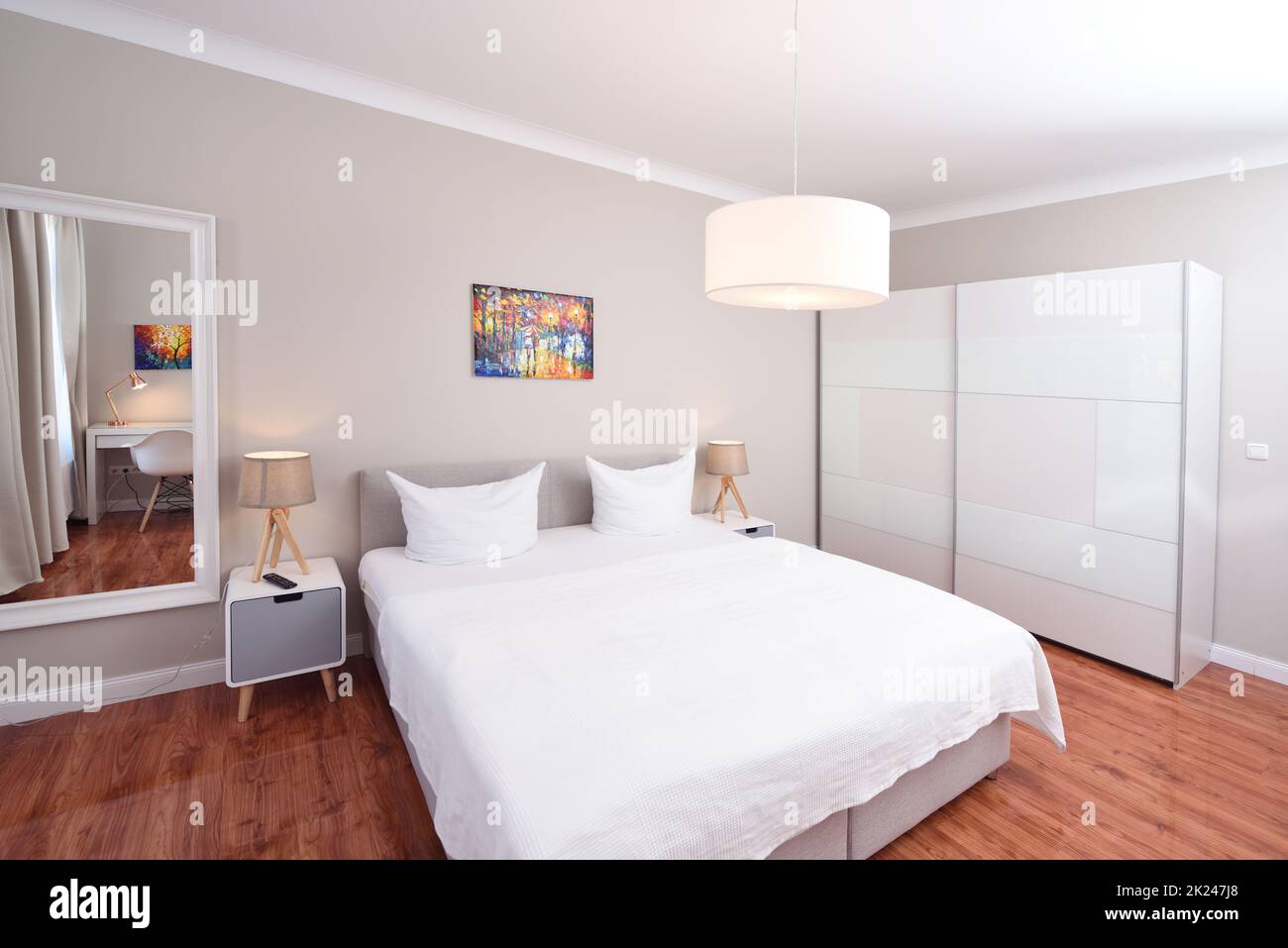 Heim Schlafzimmer Innenraum weißes Bett Holzboden Tür zum Flur buntes Bild zwei Lampen und Kissen, Spiegel Schreibtisch Stockfoto