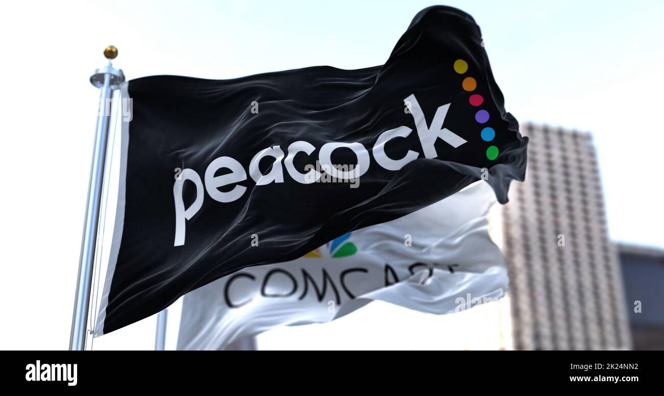 New York, USA, 2022. Januar: Die Flagge des „The Pacock TV“ winkt im Wind mit der Comcast-Flagge im Hintergrund. Pfau ist ein amerikanischer Video-Streaming-ser Stockfoto