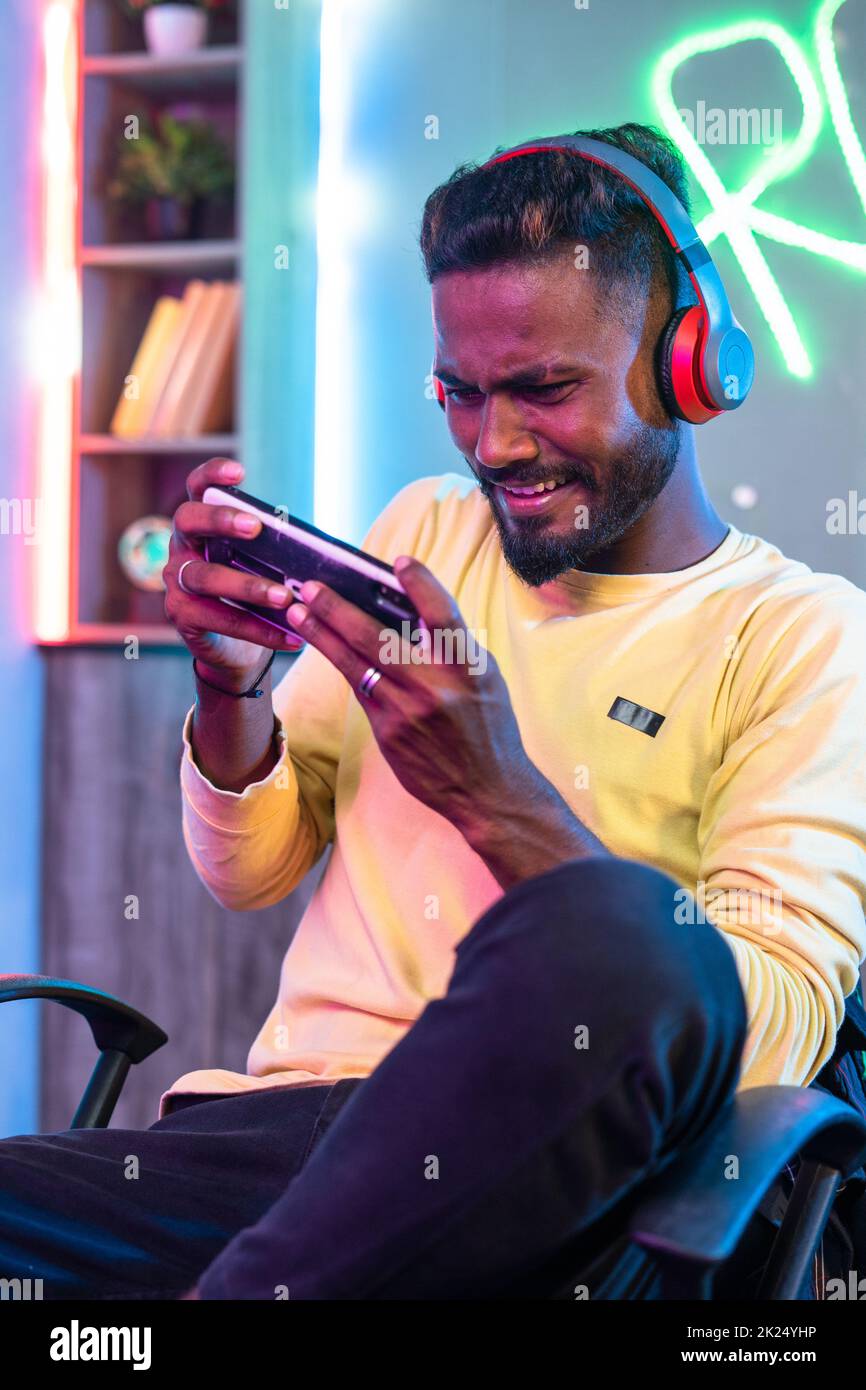 Vertikale Aufnahme eines begeisterten Spielers mit einem Headset, das Videospiele auf dem Mobiltelefon zu Hause über schnurlose Kopfhörer abspielt – Konzept der Unterhaltung Stockfoto
