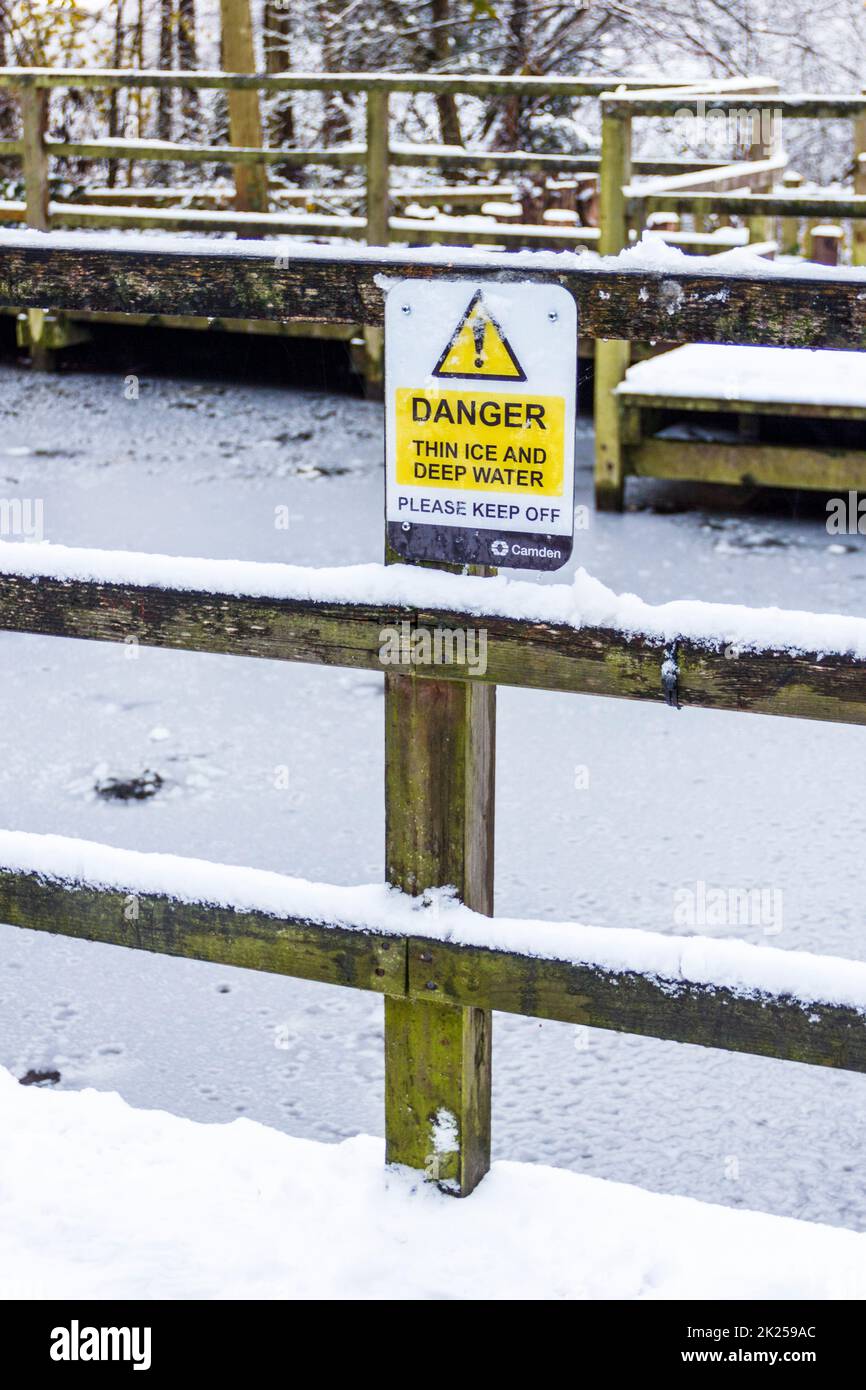 Ein Schild an einem gefrorenen Teich in einem Londoner Park, das vor dünnem Eis und tiefem Wasser warnt, North London, Großbritannien Stockfoto