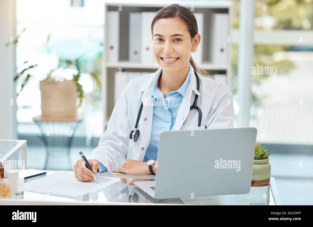 Gesundheitswesen, Medizin und ein Arzt, der auf einem Versicherungsdokument oder einer Patientenakte schreibt. Glückliche Frau, die im medizinischen Bereich arbeitet, am Schreibtisch mit Laptop-Beratung Stockfoto