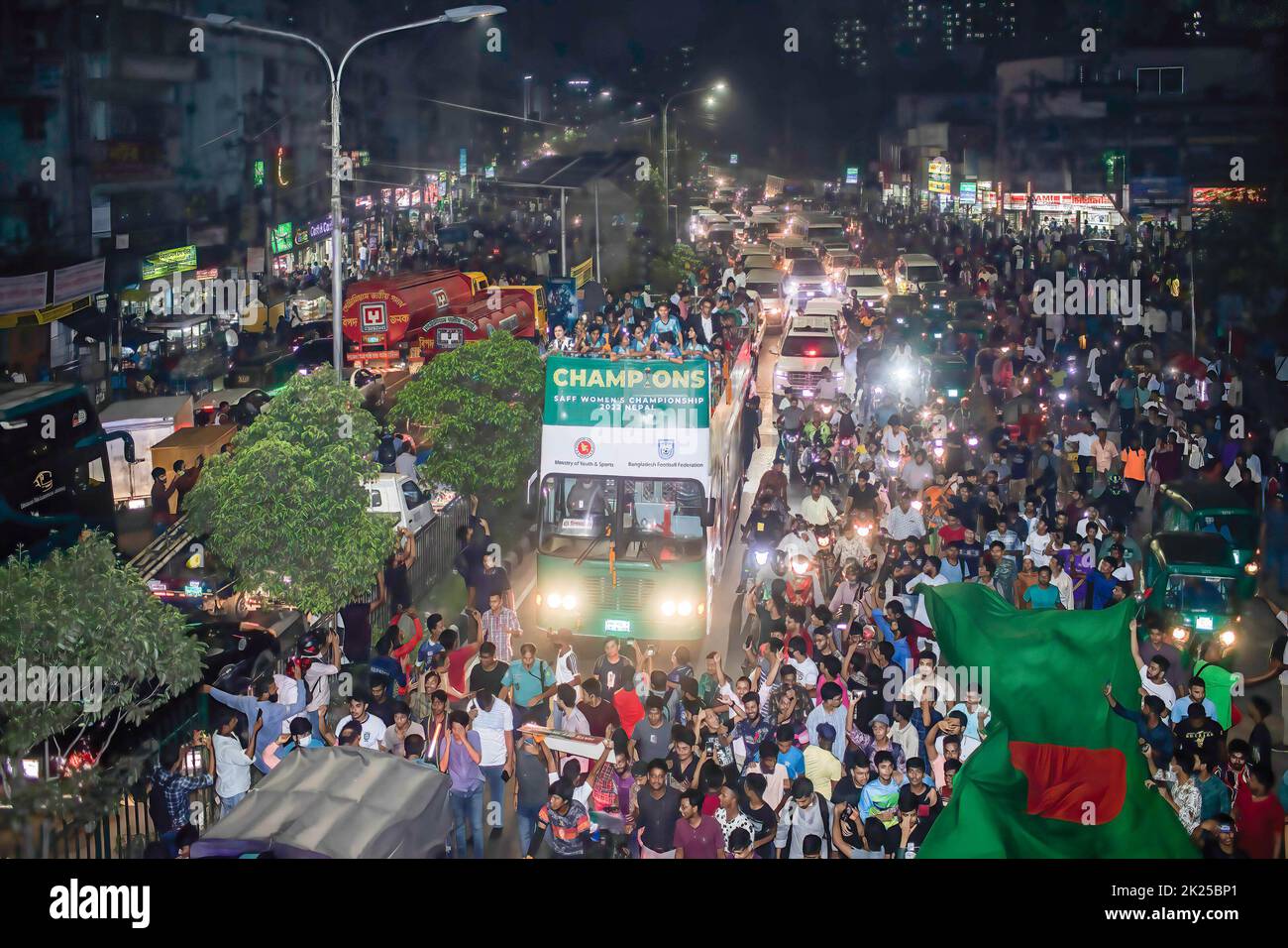 Die Fußballnationalmannschaft der Frauen feiert auf dem Weg zum Bangladesh Football Federation House. Die bangladeschische Fußballnationalmannschaft der Frauen hält die Trophäe der SAFF-Frauenmeisterschaft in einem offenen Bus auf dem Weg vom internationalen Flughafen Hazrat Shahjalal zum BFF-Haus ab, während Tausende von einfachen Menschen die Spieler am Straßenrand begrüßen. Stockfoto