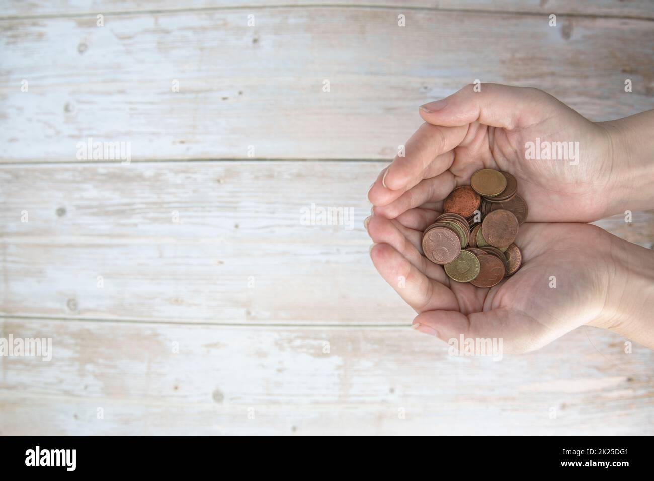 Hände, die einen Haufen Euro-Münzen in der Hand halten, auf Holzhintergrund. Spenden, Sparen, Spendenaktionen, Familienfinanzplan, Finanzkrisenkonzept. Draufsicht. Speicherplatz kopieren Stockfoto