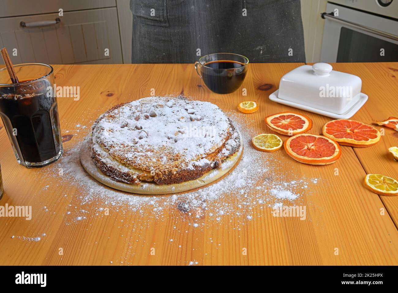 Man streut Puderzucker auf hausgemachten Kuchen. Ein Holztisch und Küche Hintergrund Stockfoto