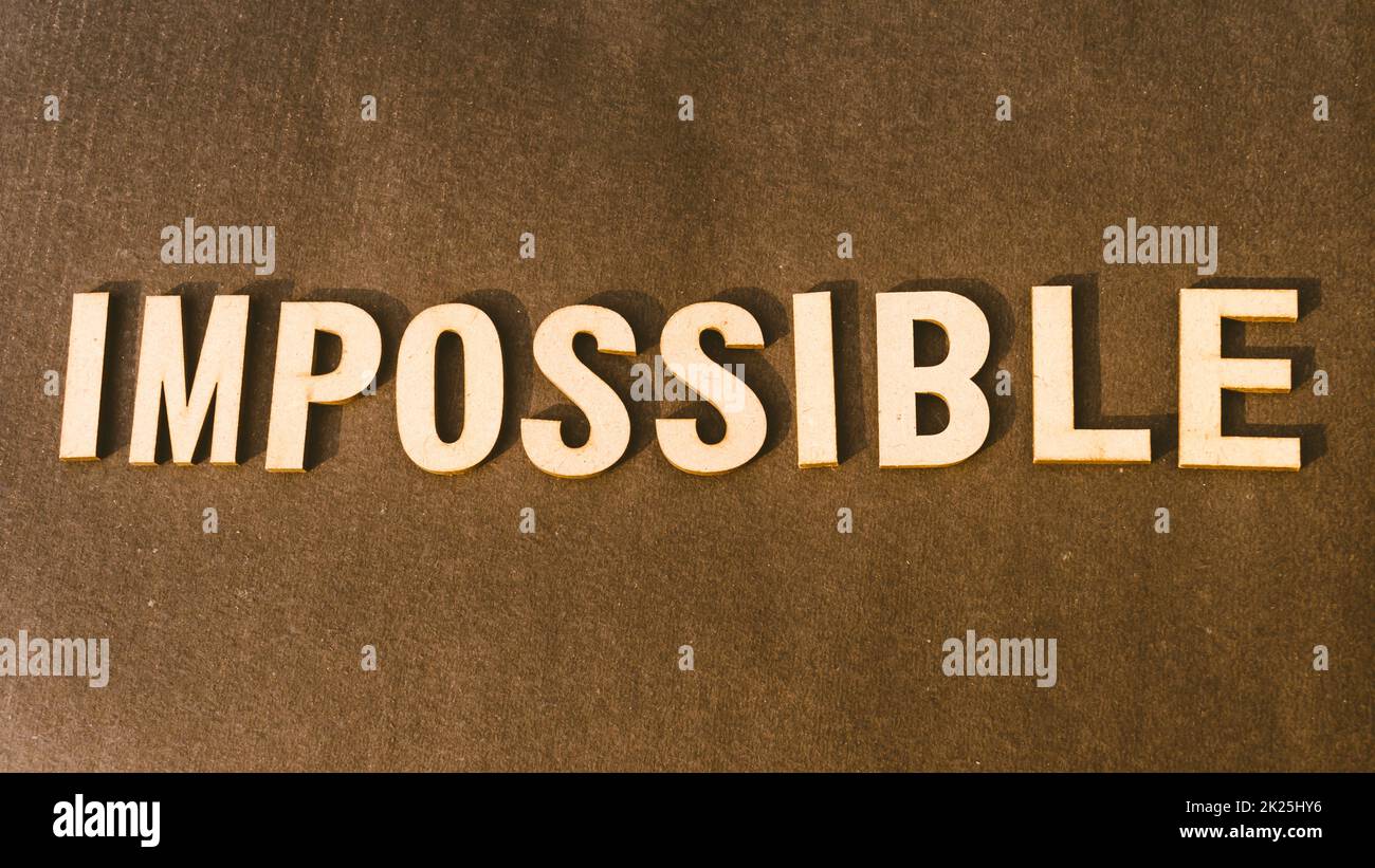 Das Wort Impossible wurde mit dem Stempel „Brown Wooden Alphabet“ auf Vintage-Hintergrund geschrieben. Stockfoto