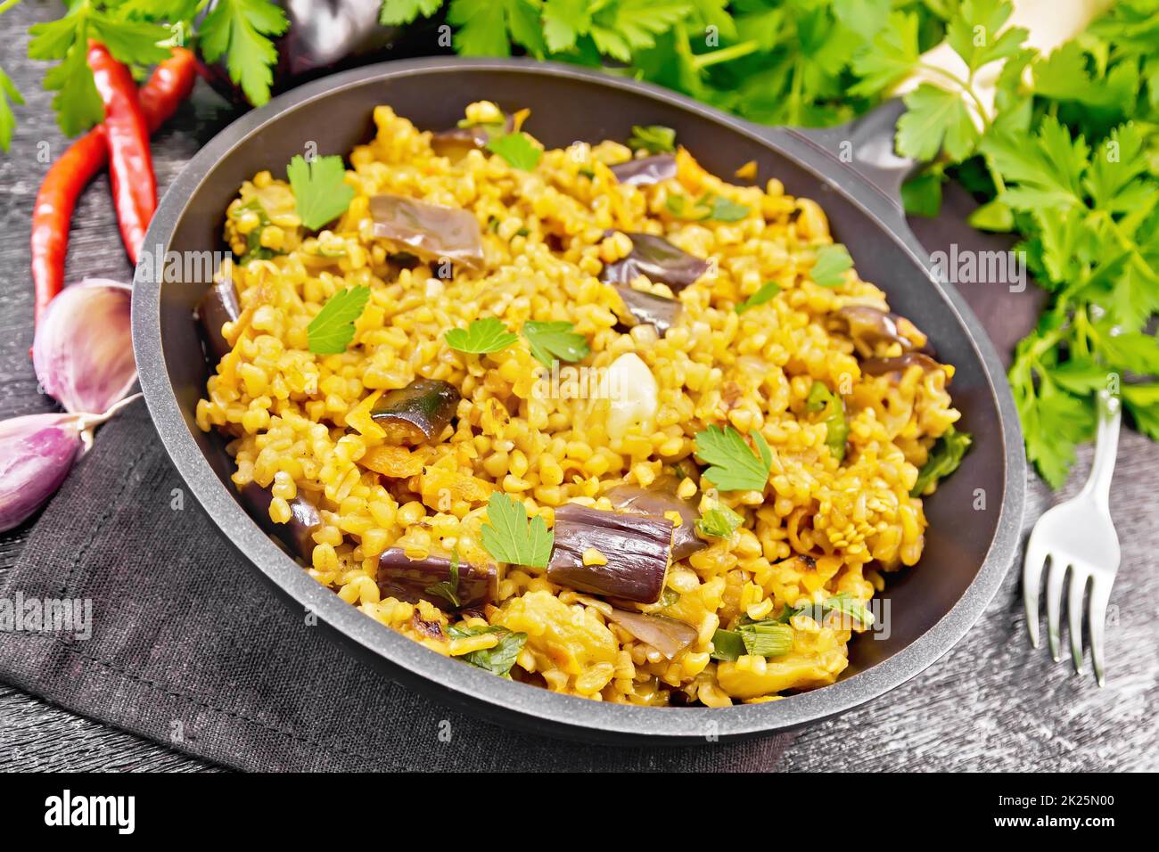 Bulgur mit Aubergine in der Pfanne auf schwarzem Brett Stockfoto