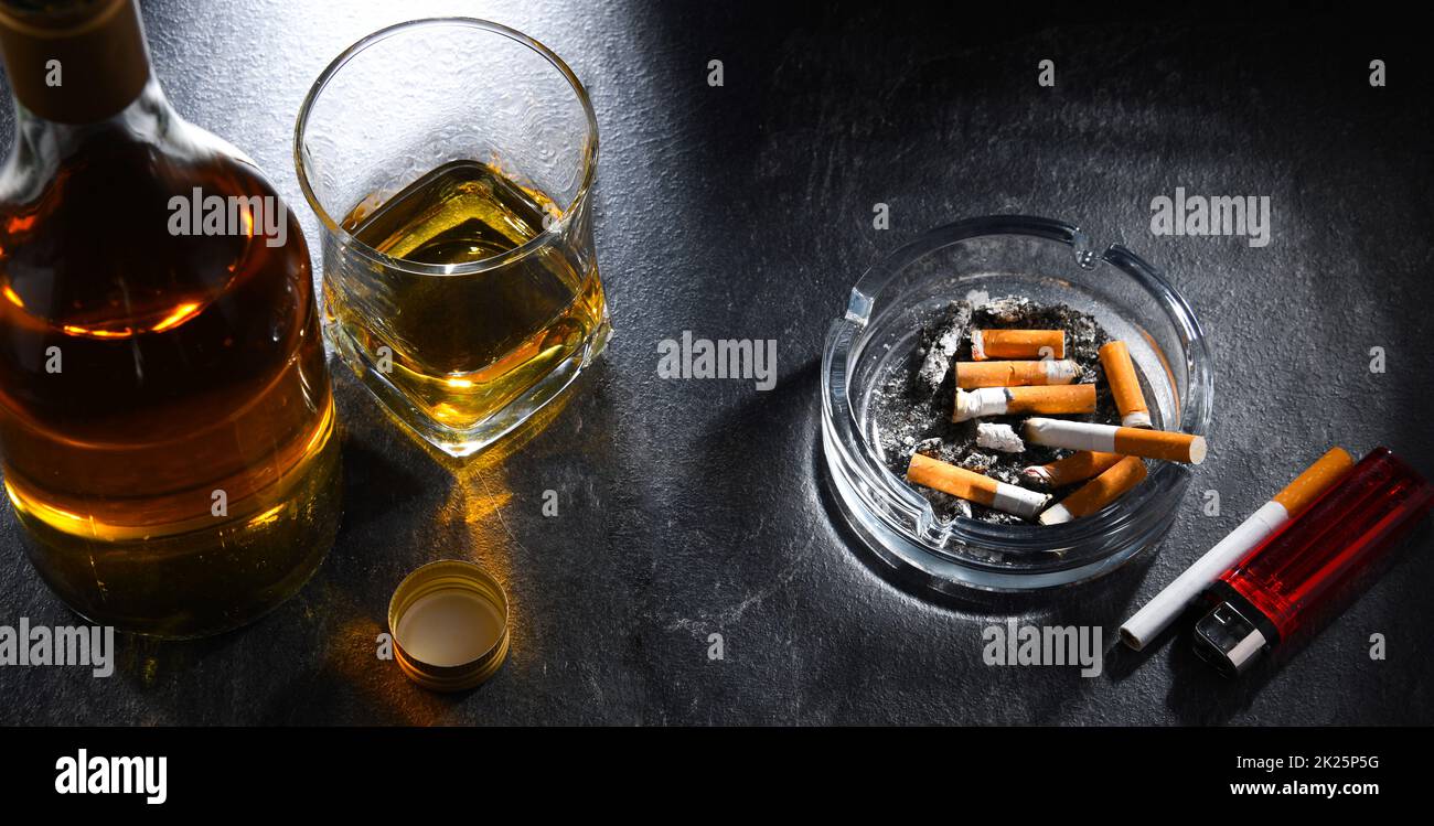 Zusammensetzung mit einer Flasche Whiskey, einem Aschenbecher und Zigaretten Stockfoto