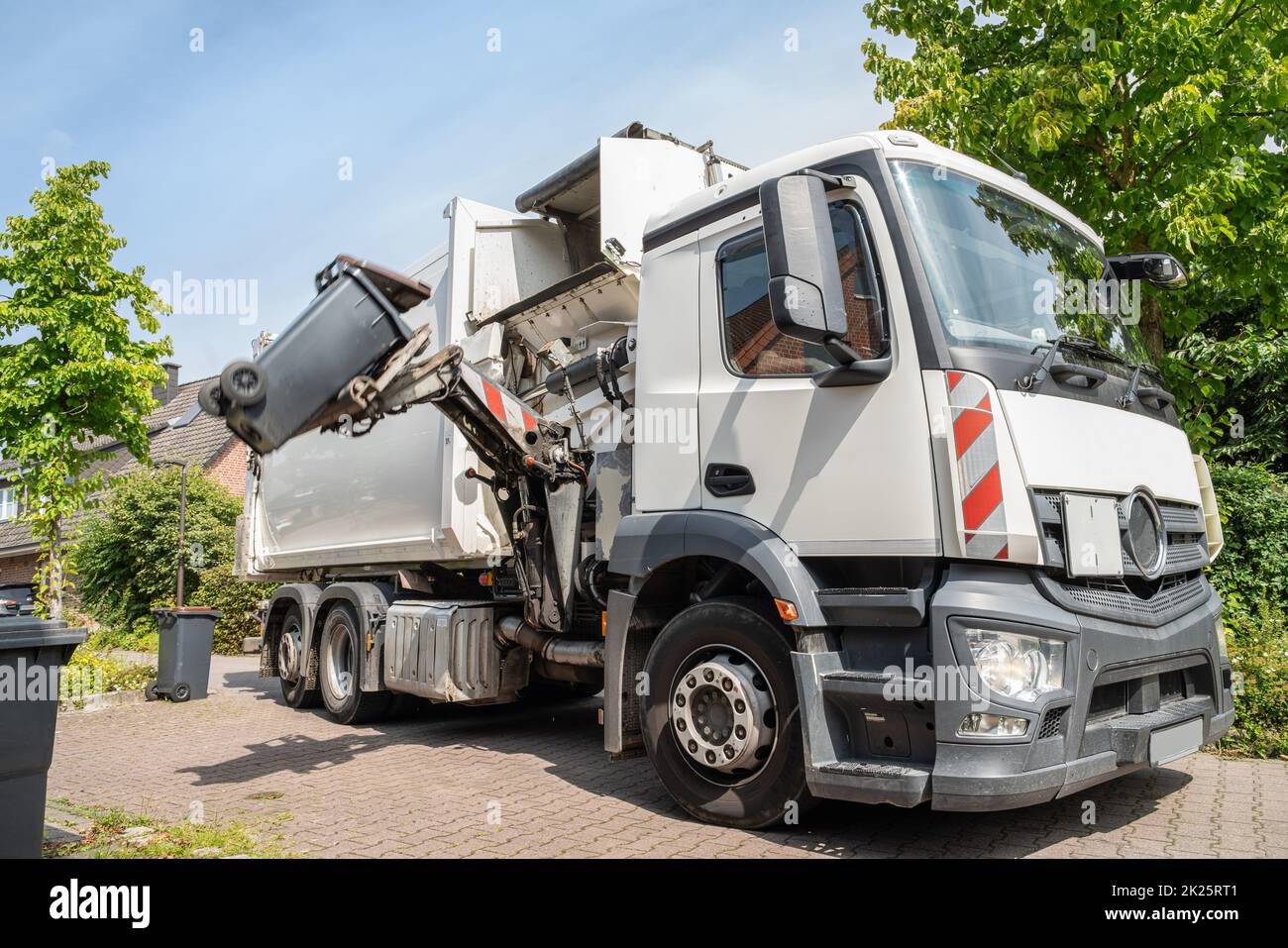 Automatische Müllabfuhr - hydraulischer Seitenlader eines weißen Müllwagens greift die Mülltonne, um sie zu entleeren Stockfoto