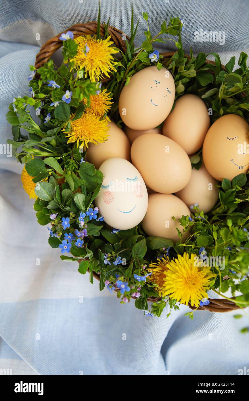 Wunderschönes Frühlingsbouquet in einem Holzkorb mit Osterbemalung, Eiern mit süßen Gesichtern. Osterpostkarte. Stockfoto