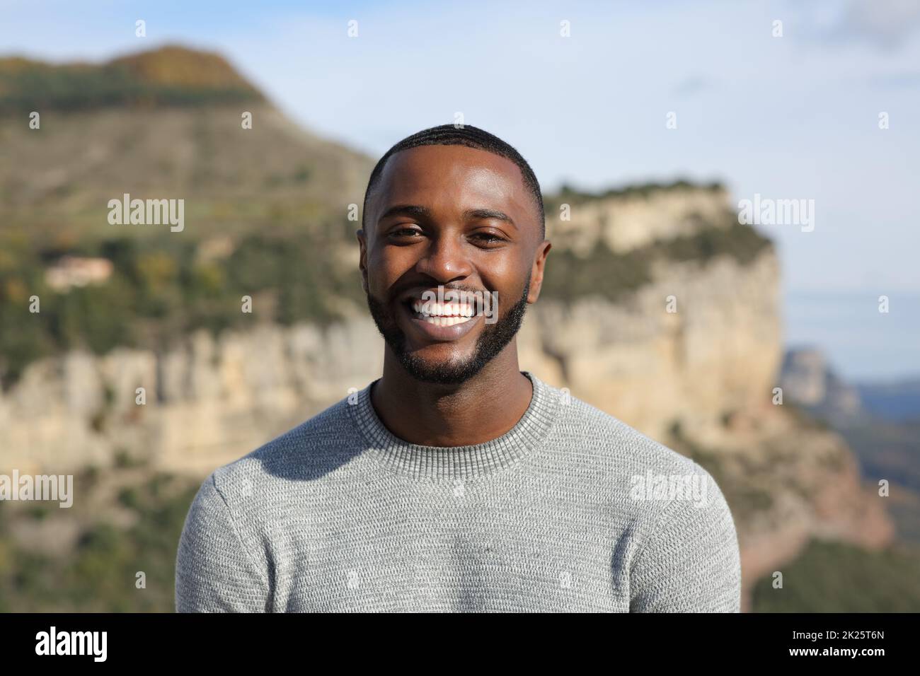 Glücklicher Mann mit schwarzer Haut, der in den Bergen vor der Kamera lächelt Stockfoto