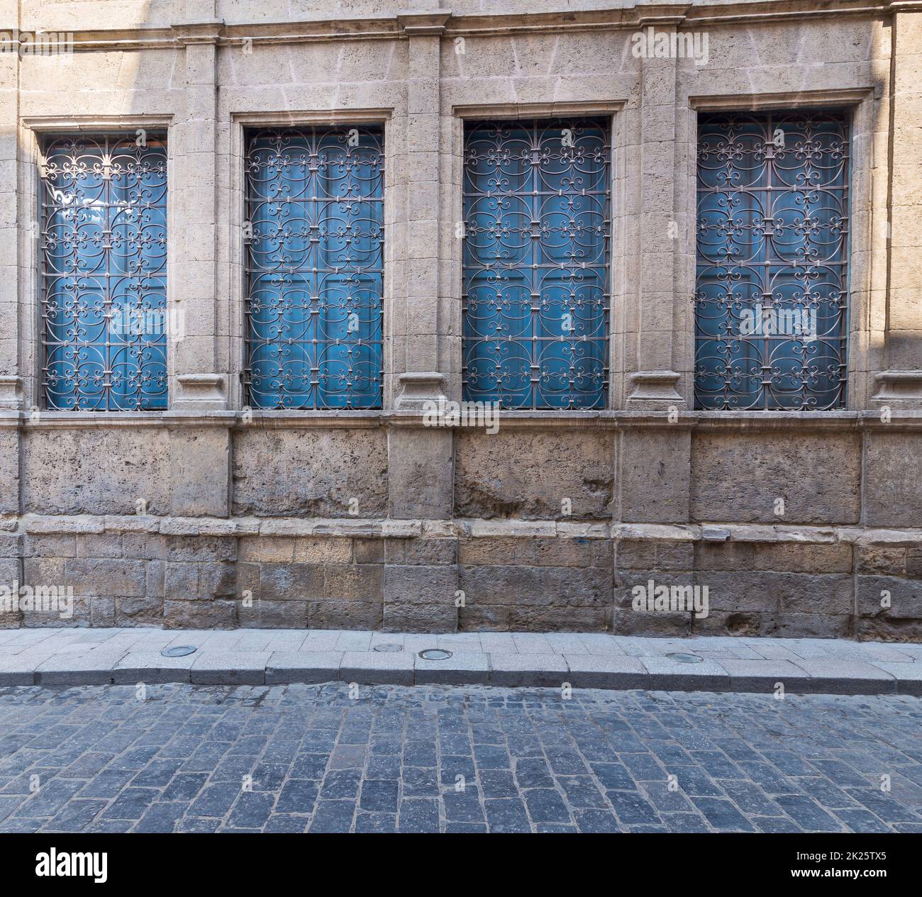 Fenster mit schmiedeeisernem Grill und blauen Fensterläden an alten Steinmauern und Basaltstraße Stockfoto
