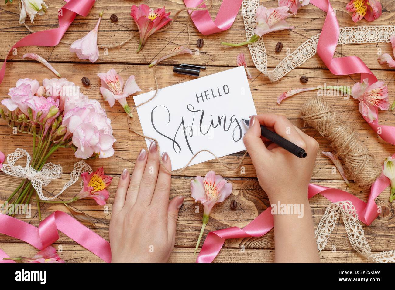Die Hände schreiben eine romantische „HELLO SPRING“-Karte zwischen rosa Blumen Stockfoto