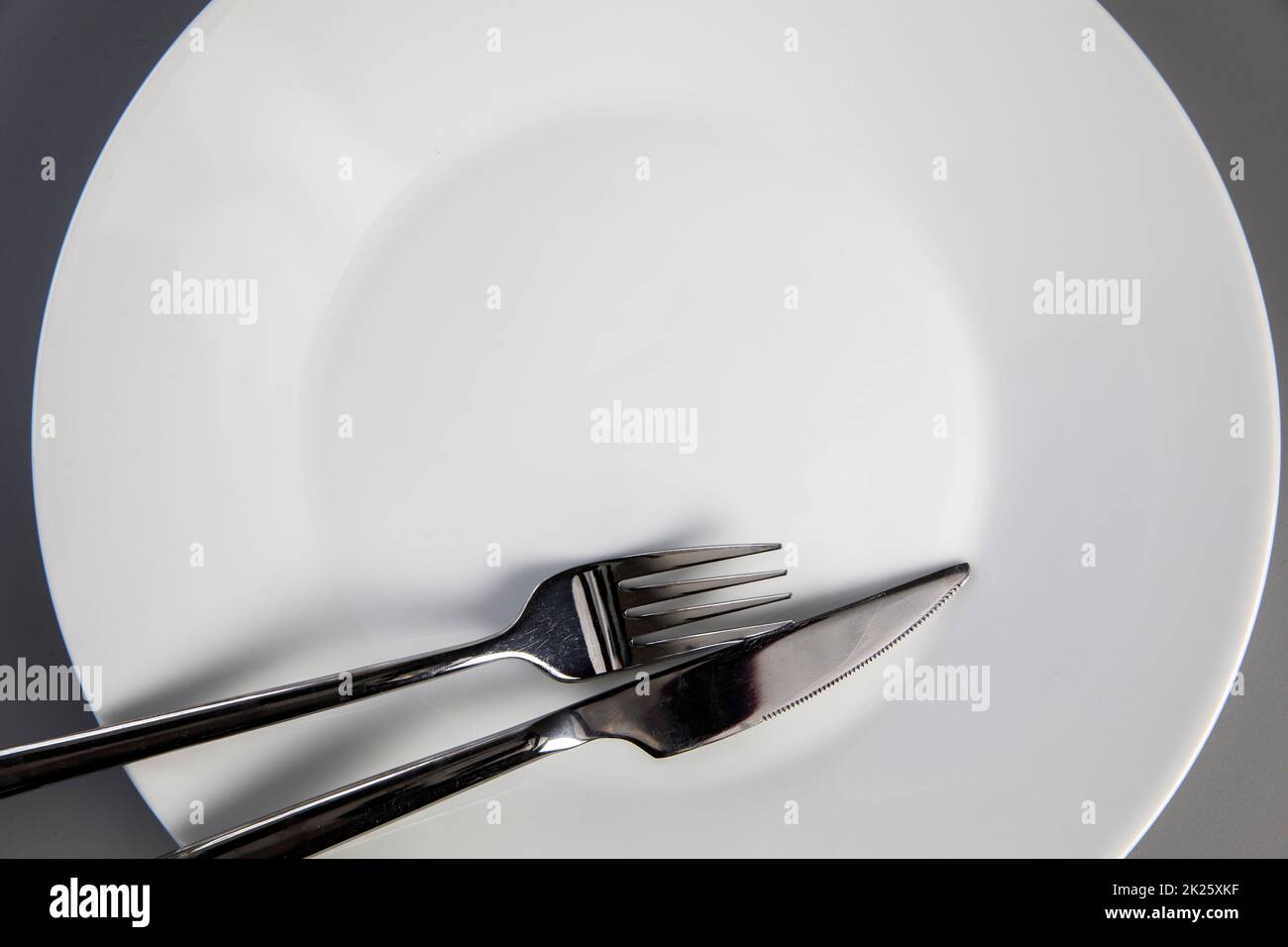 Leerer Teller mit Gabel und Messer auf grauem Hintergrund, Draufsicht für Kopierraum, Lebensmittel und gesundes Essenskonzept Stockfoto