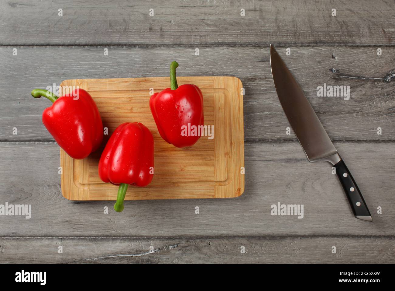 Tischplatte, 3 rote Paprika, mit Wasser besprüht, bereit, auf Schneidebrett schneiden, mit Chef Messer an der Seite. Stockfoto