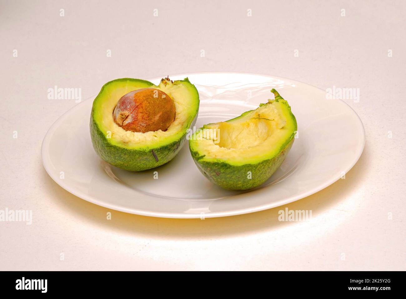 Reife Avocado auf Keramikplatte, in zwei Hälften geschnitten Stockfoto