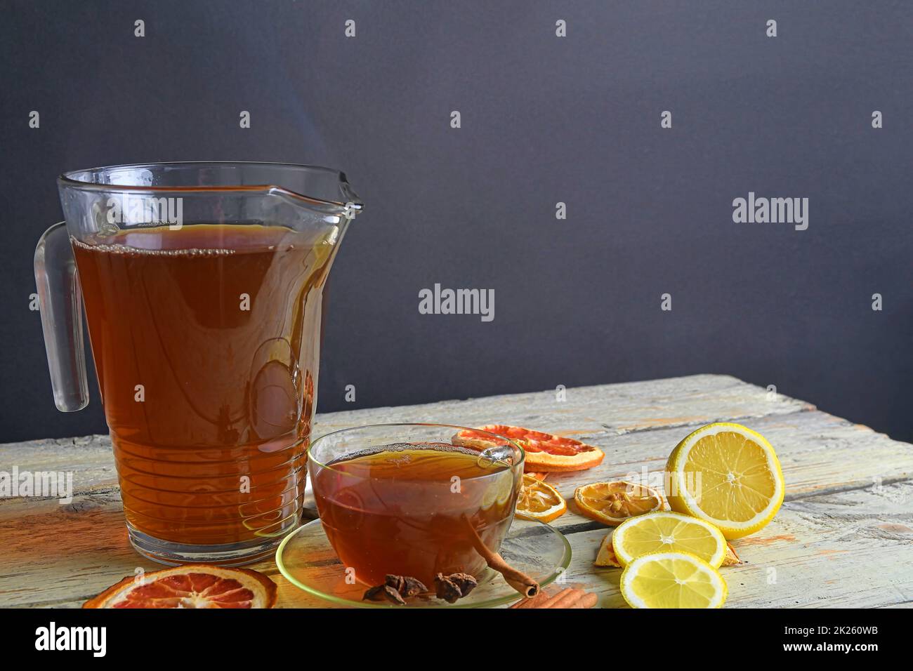 Warme Tasse Tee und Glaskanne auf rustikalem Holztisch. Zimtstangen, Sternanis, Zitrone und getrocknete Früchte. Schwarzer Hintergrund mit Kopierbereich. Stillleben-Konzept Stockfoto