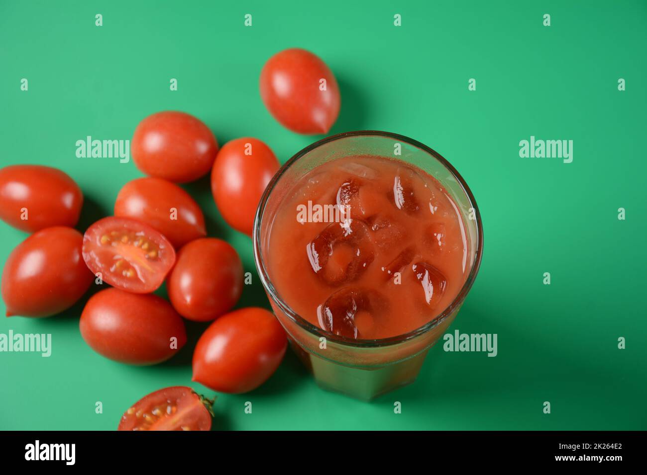 Volles Glas frischen Tomatensaft mit Kirschtomaten herum. Sehr schmackhafter und gesunder Tomatensaft mit Eiswürfeln Stockfoto
