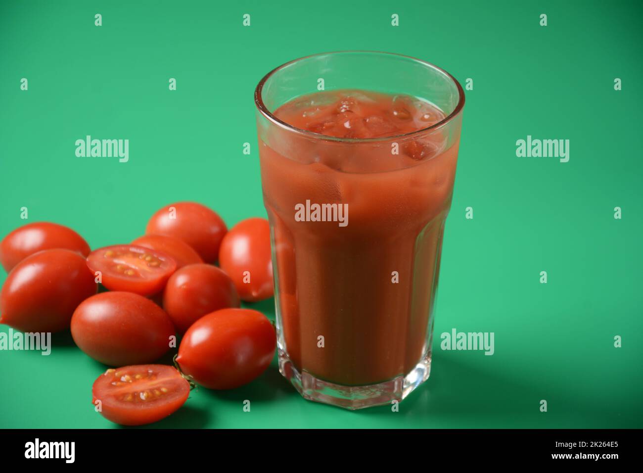 Volles Glas frischen Tomatensaft mit Kirschtomaten herum. Sehr schmackhafter und gesunder Tomatensaft mit Eiswürfeln Stockfoto