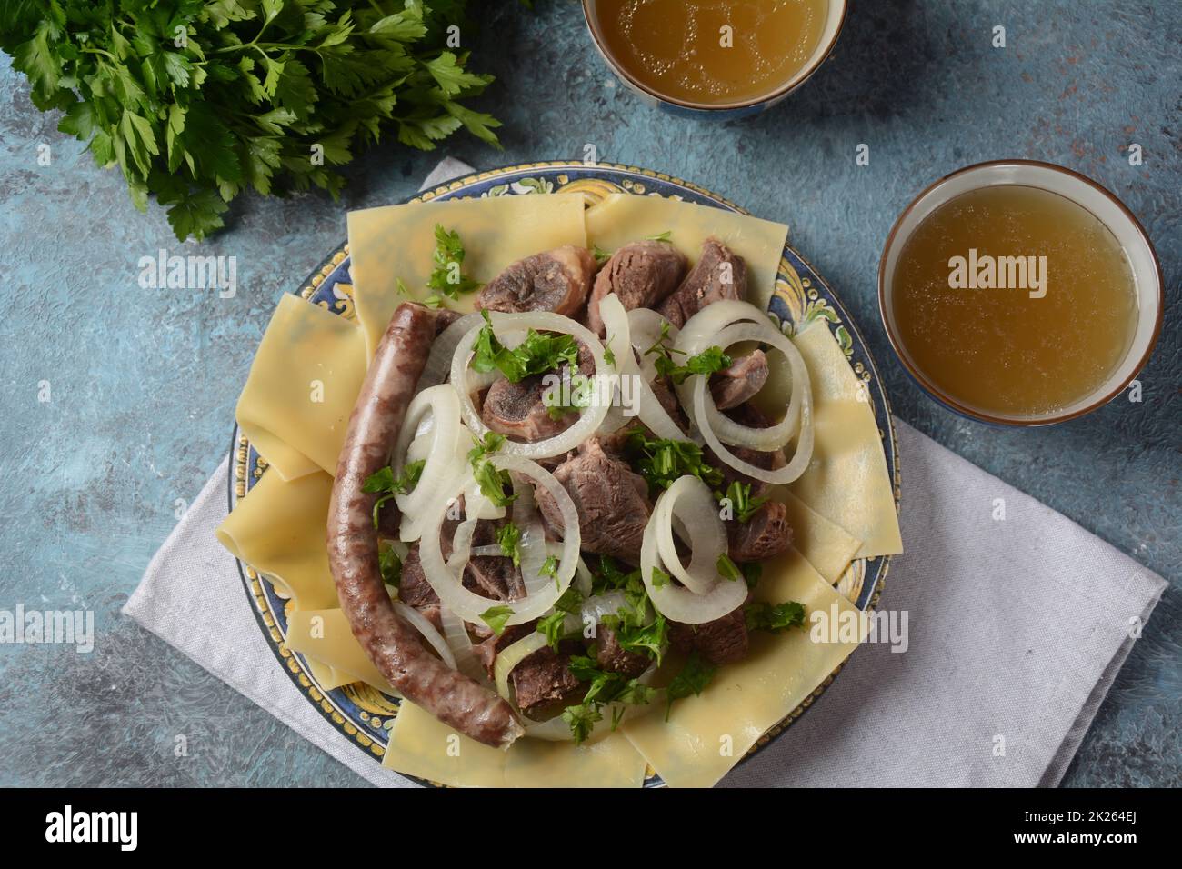 Beshbarmak – Kasachisches Nationalgericht, zubereitet mit Fleisch und Nudeln. Nahaufnahme des Schüssels Beshbarmak auf einem Teller auf dem Tisch. Große Stücke gedünstetes Fleisch und Zwiebeln Stockfoto