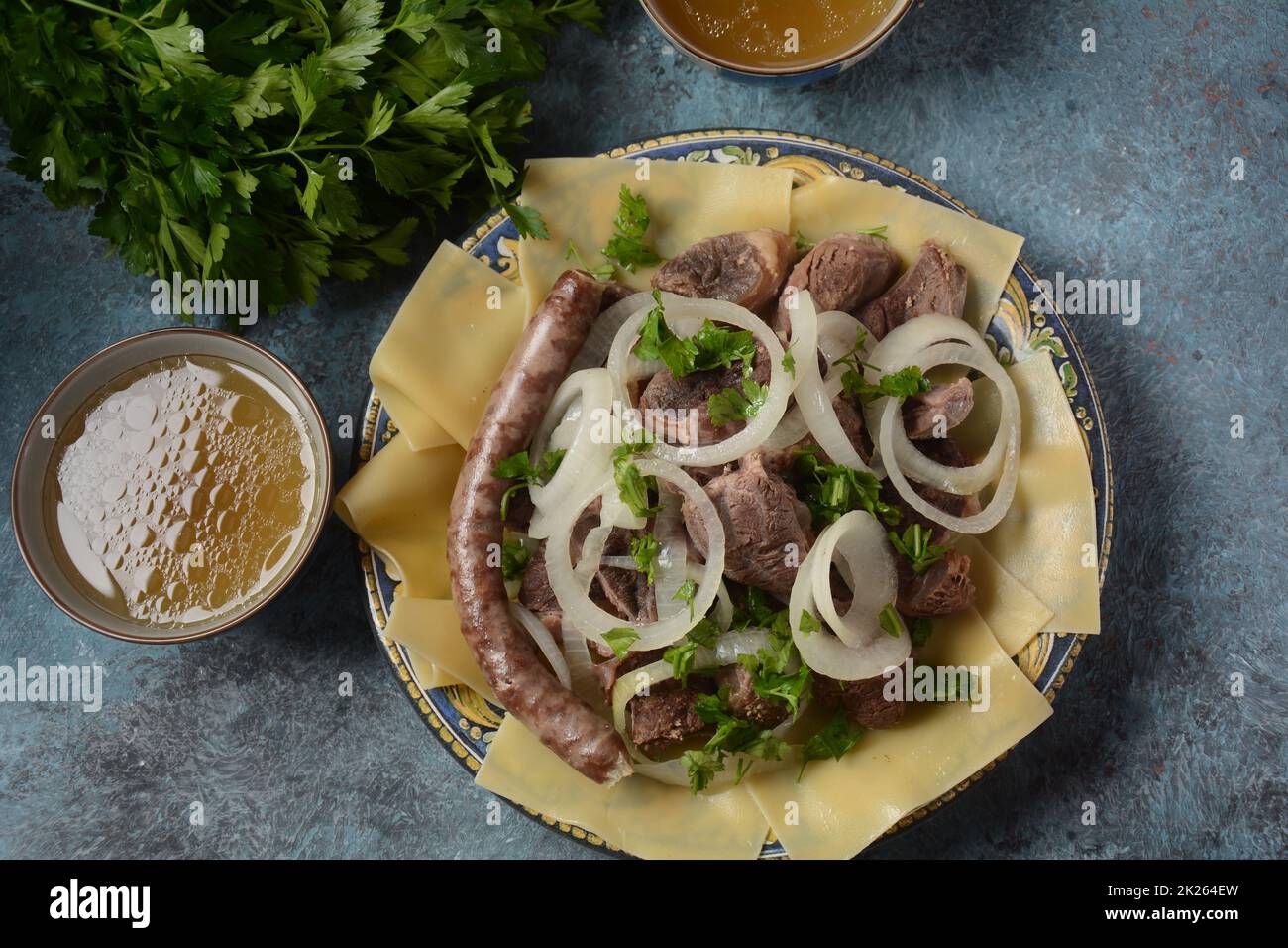 Beshbarmak – Kasachisches Nationalgericht, zubereitet mit Fleisch und Nudeln. Nahaufnahme des Schüssels Beshbarmak auf einem Teller auf dem Tisch. Große Stücke gedünstetes Fleisch und Zwiebeln Stockfoto