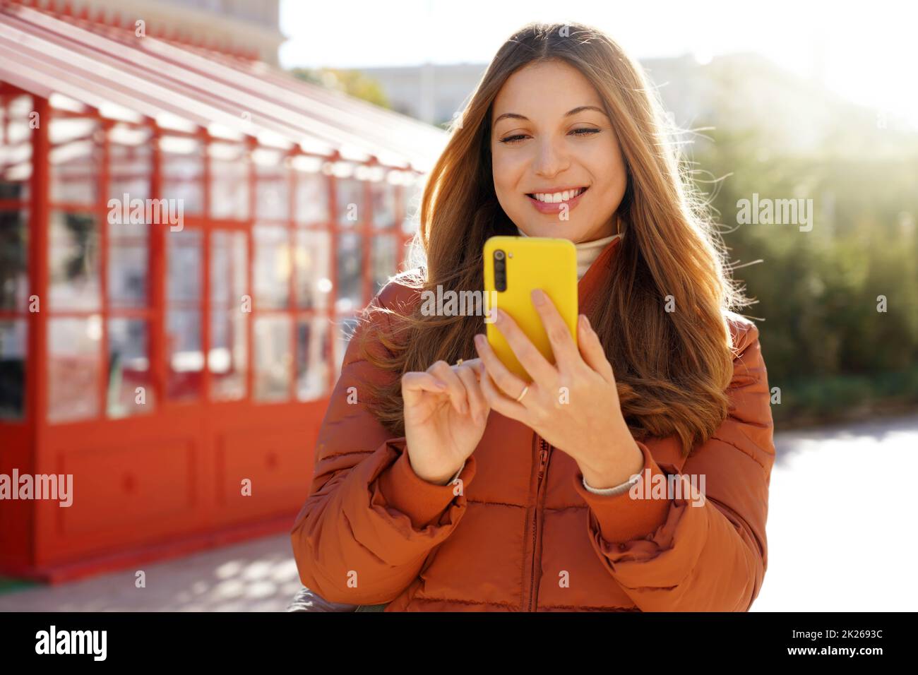 Schöne lächelnde Frau in Kugeljacke hält Smartphone im Winter Zeit Stockfoto