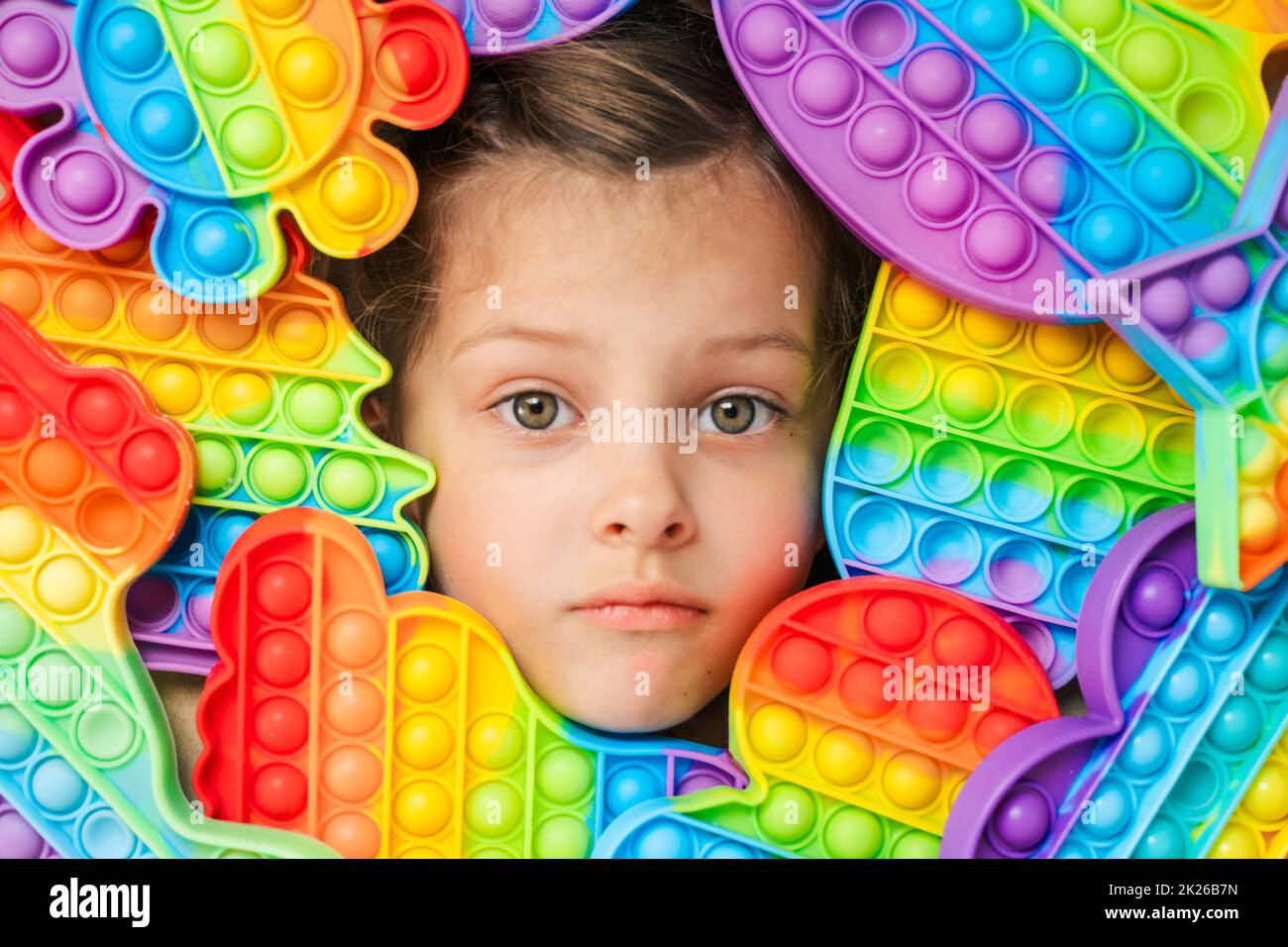 Kleines Mädchen, Kind, Kind Kopf unter vielen, viele bunte Pop it. Kinder spielen. Trendy Silikon Antistress bunte sensorische Push-Spielzeug popit. Flatterndes fid Stockfoto