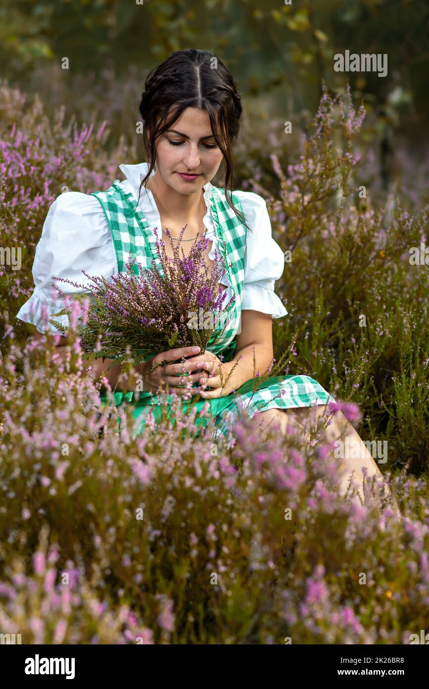 Frau im Dirndl sitzt in der Heide Stockfoto