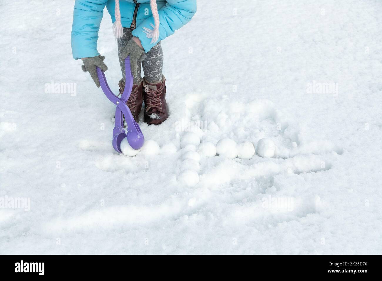 Das Kind hat Spaß beim Basteln von Schneebällen mit dem Spielzeugkunststoffautomaten. Kinder, die Schneebälle zwischen den Schneeverwehungen spielen. Platz für Text. Stockfoto