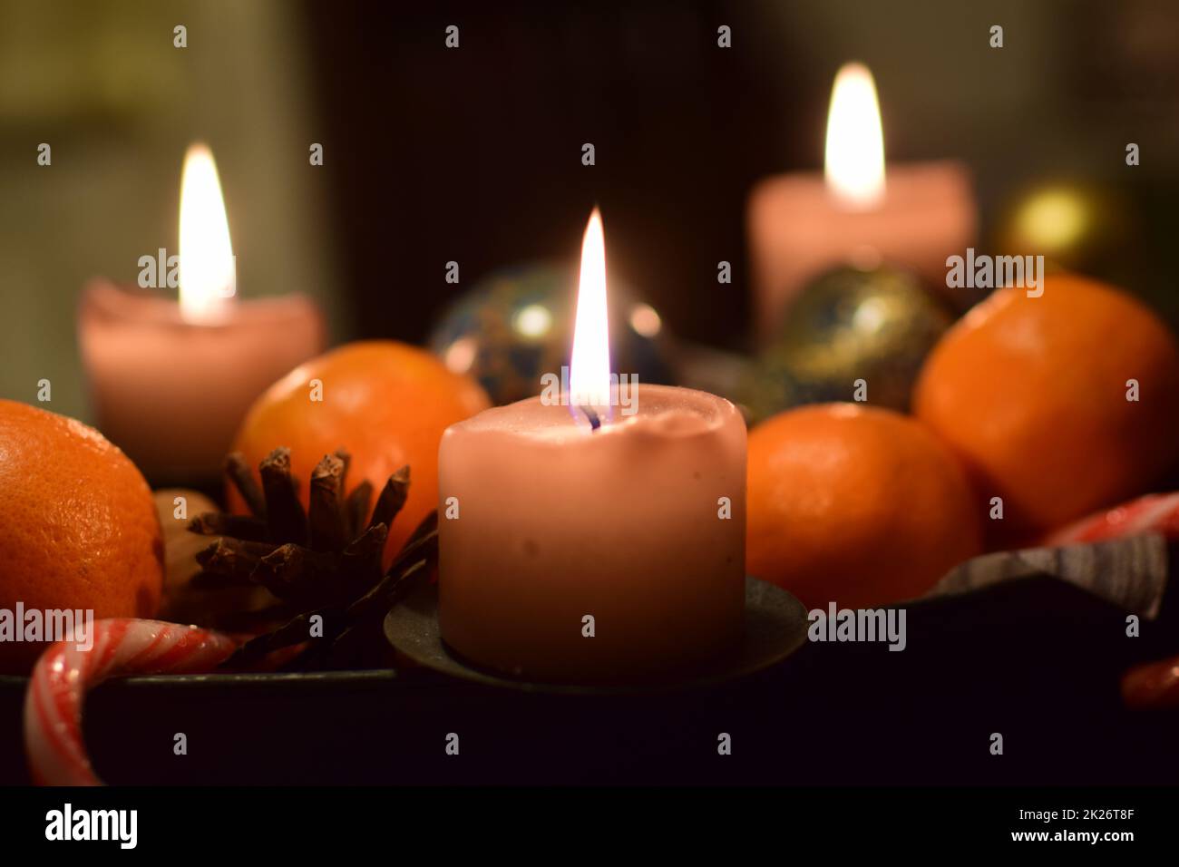 Drei brennende Kerzen mit Manadarinen und einem Pinienkegel als weihnachtsdekoration Stockfoto