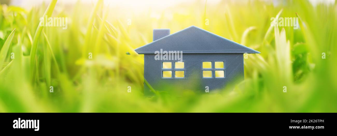 Graues Plastikmodell des Hauses auf dem frischen Gras an einem sonnigen Tag. Stockfoto